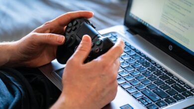 Person holds a gaming controller while interacting with a laptop, emphasizing modern gaming technology.